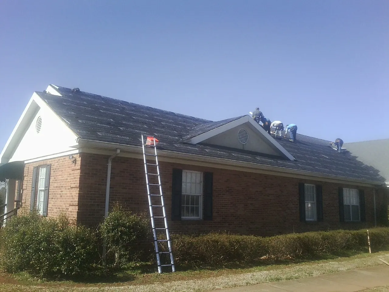 Crew tearing shingles off a brick ranch roof with a ladder set — Emergency Roof Repair work by our crew in Palo Cedro