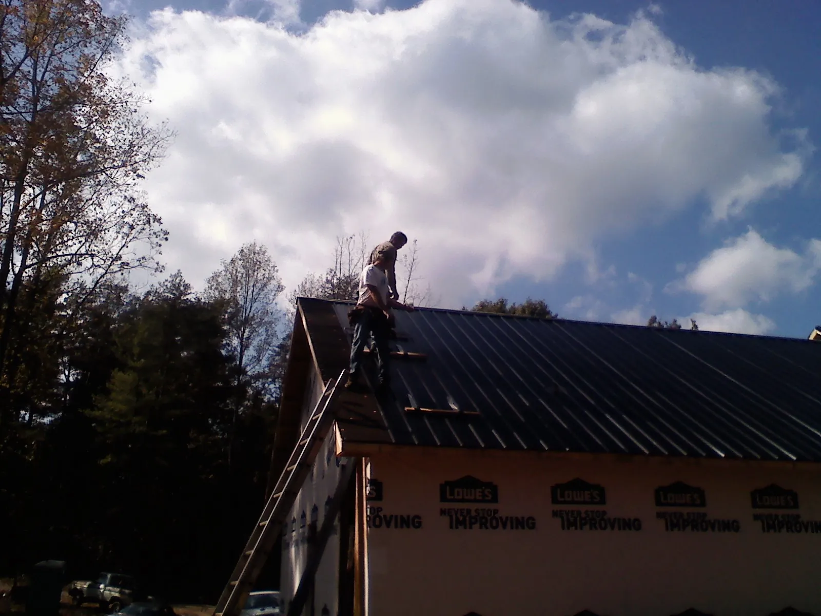 Roofer fastening dark metal panels high against a cloudy sky, from a Roof Inspection job in Palo Cedro